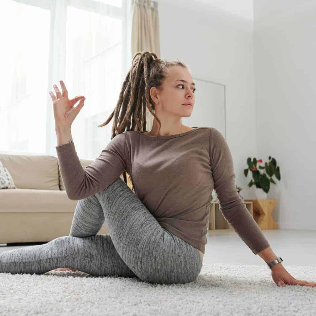 Young female with dreadlocks sitting on the floor in one of yoga positions